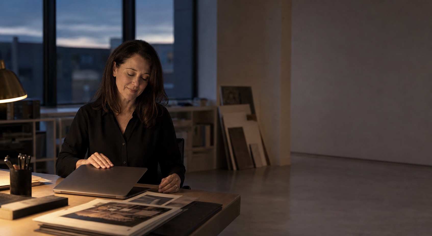 A studio principal closing her laptop at the end of the day in a quiet design studio.