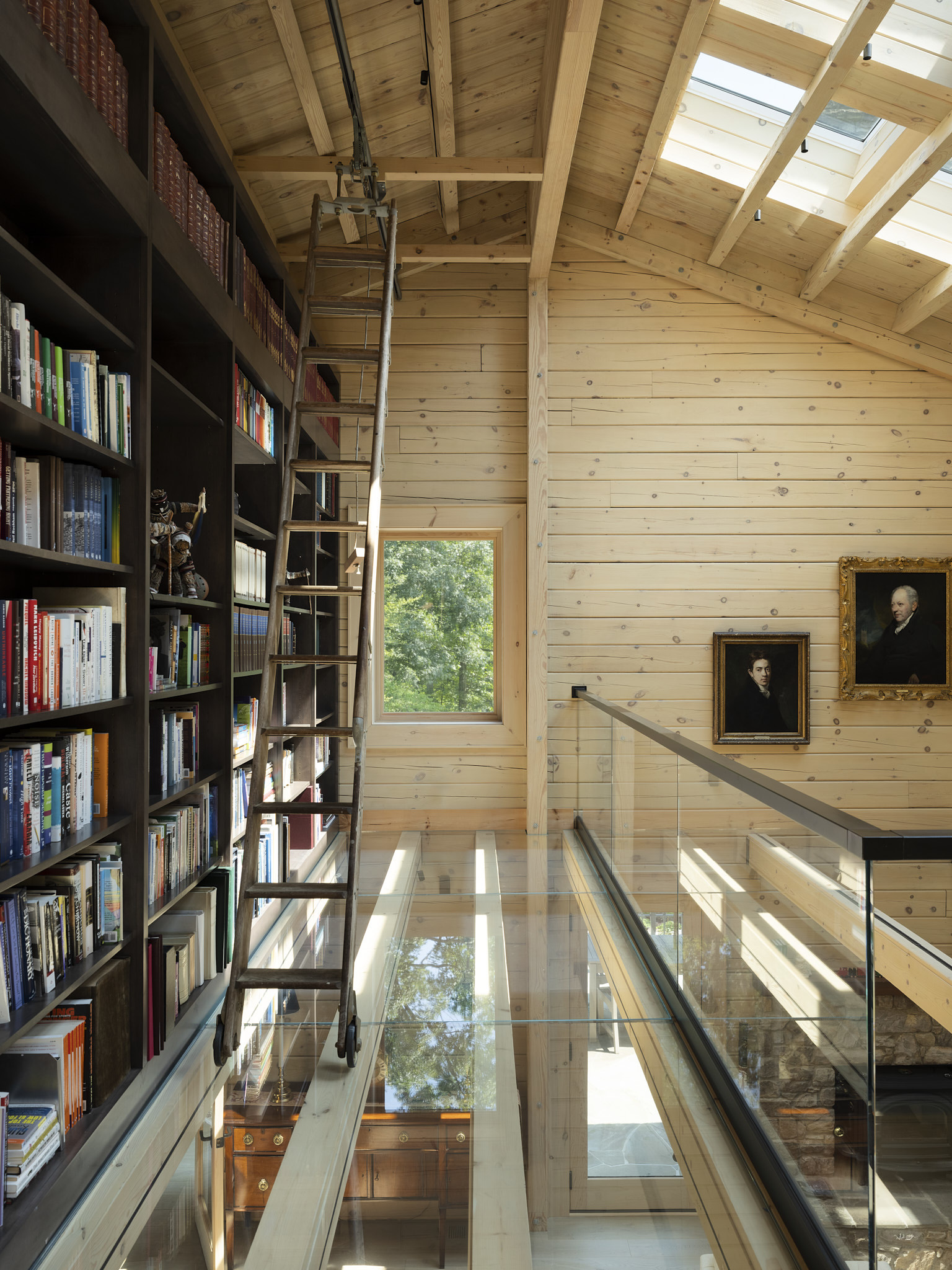 A double-height library with a rolling ladder, dark shelving and a glass-floored bridge, designed by Gruver Cooley.