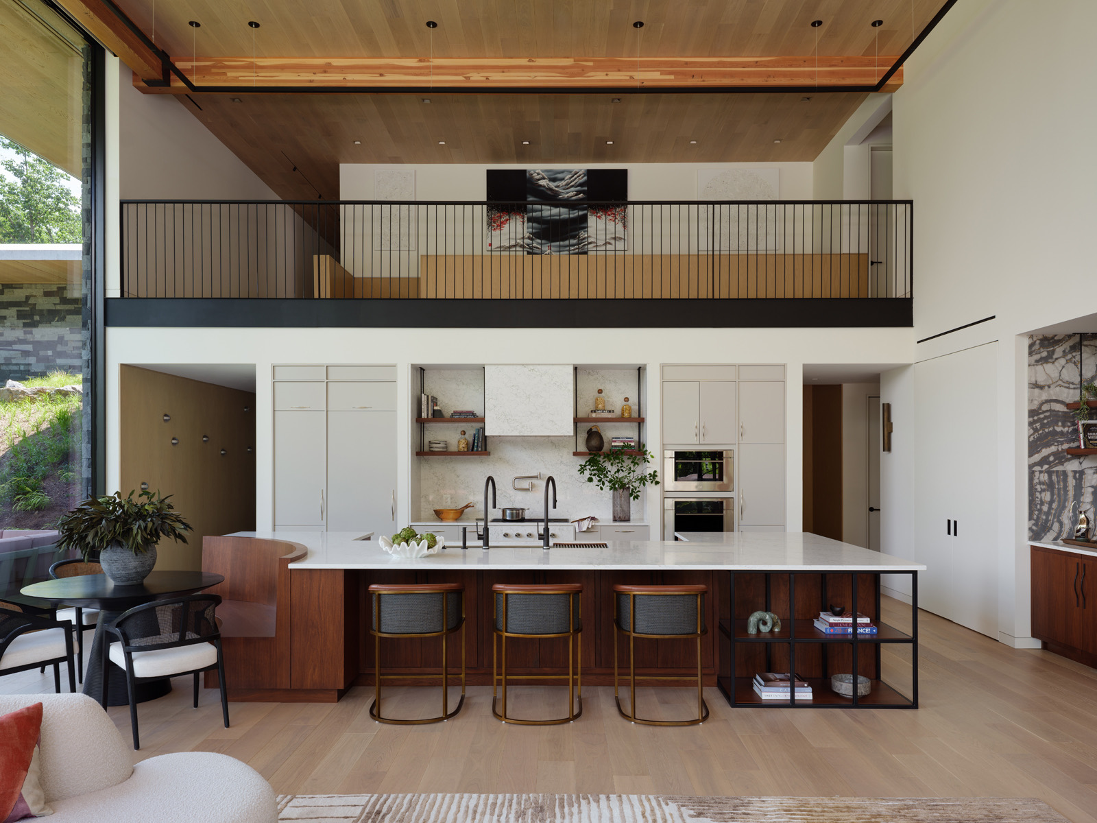 A double-height kitchen and living space with exposed timber structure, walnut millwork and a stone island, designed and built by Gruver Cooley.