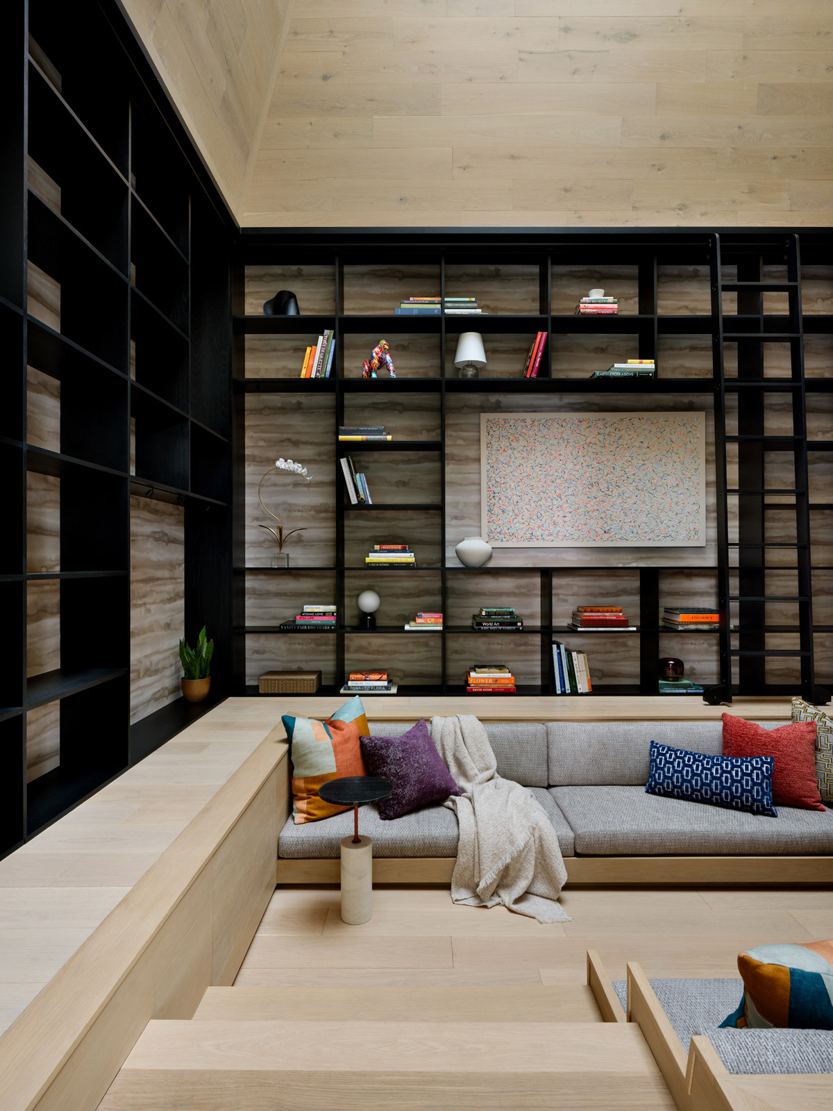 A lounge with full-height black shelving, a built-in bench and stepped oak platform, by Gruver Cooley.