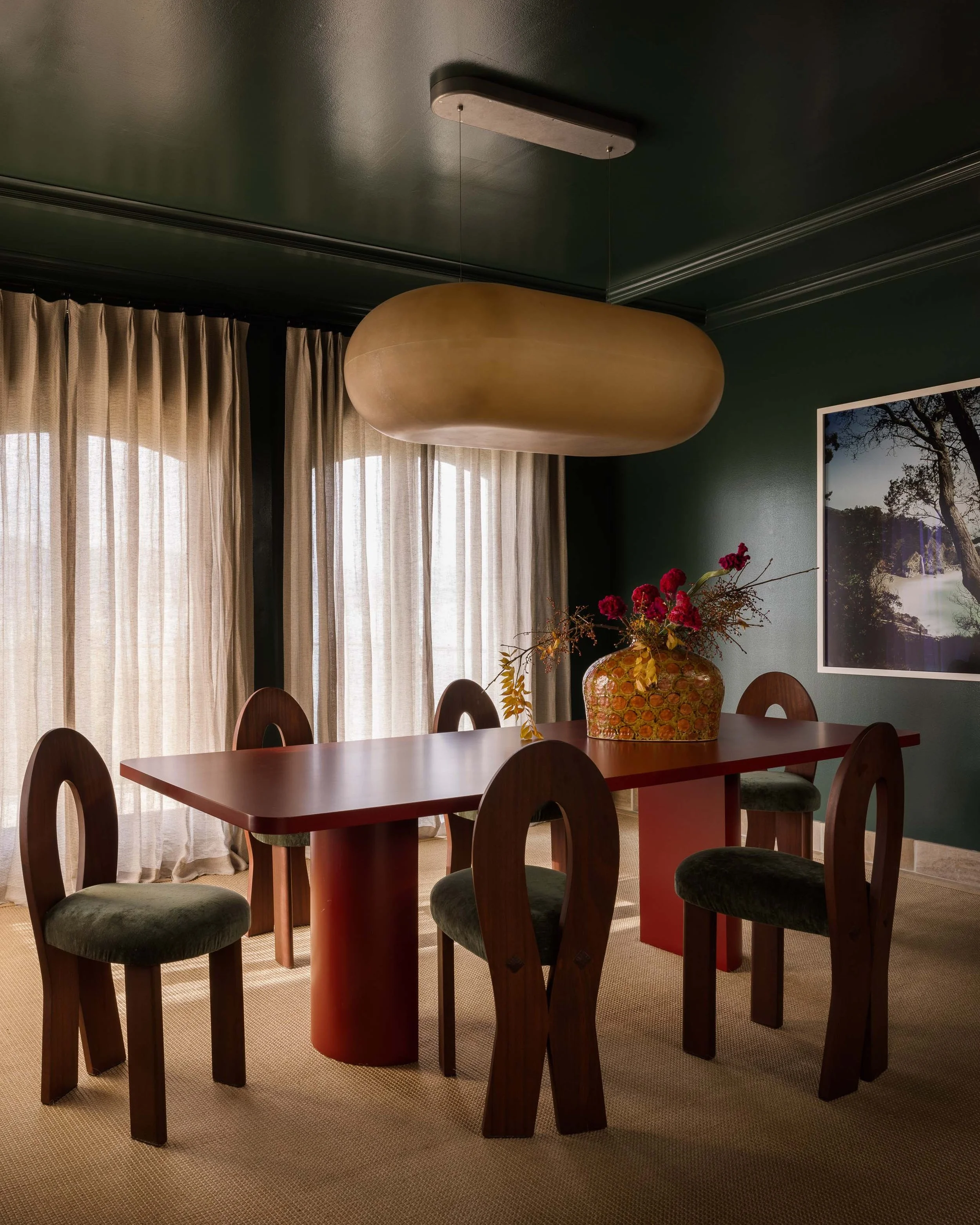 A dining room with a long table, sculptural pendant and layered textiles, designed by Studio Montemayor.