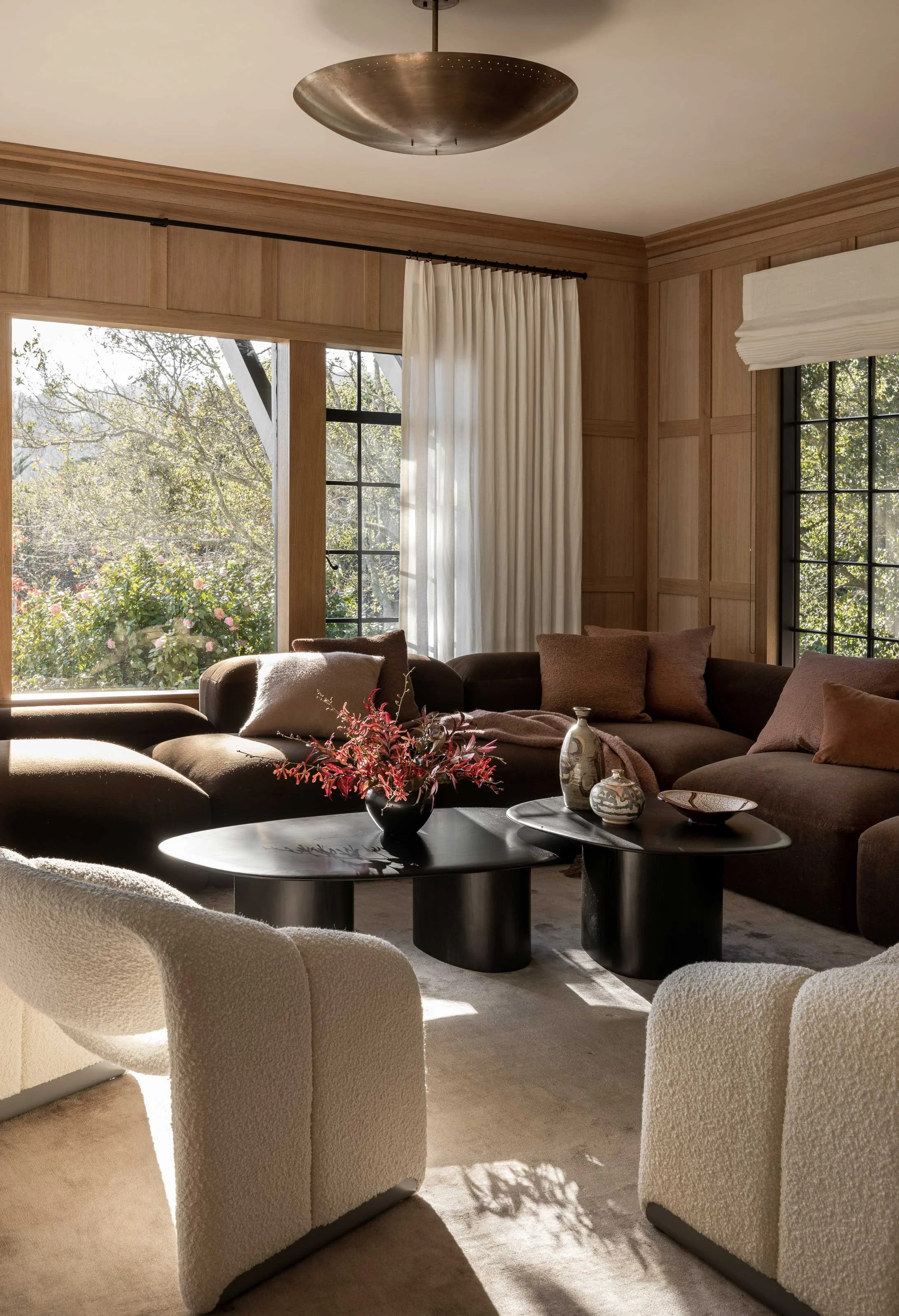A finished living room with a deep brown sectional, bouclé chairs and late afternoon light, designed by Studio Montemayor.